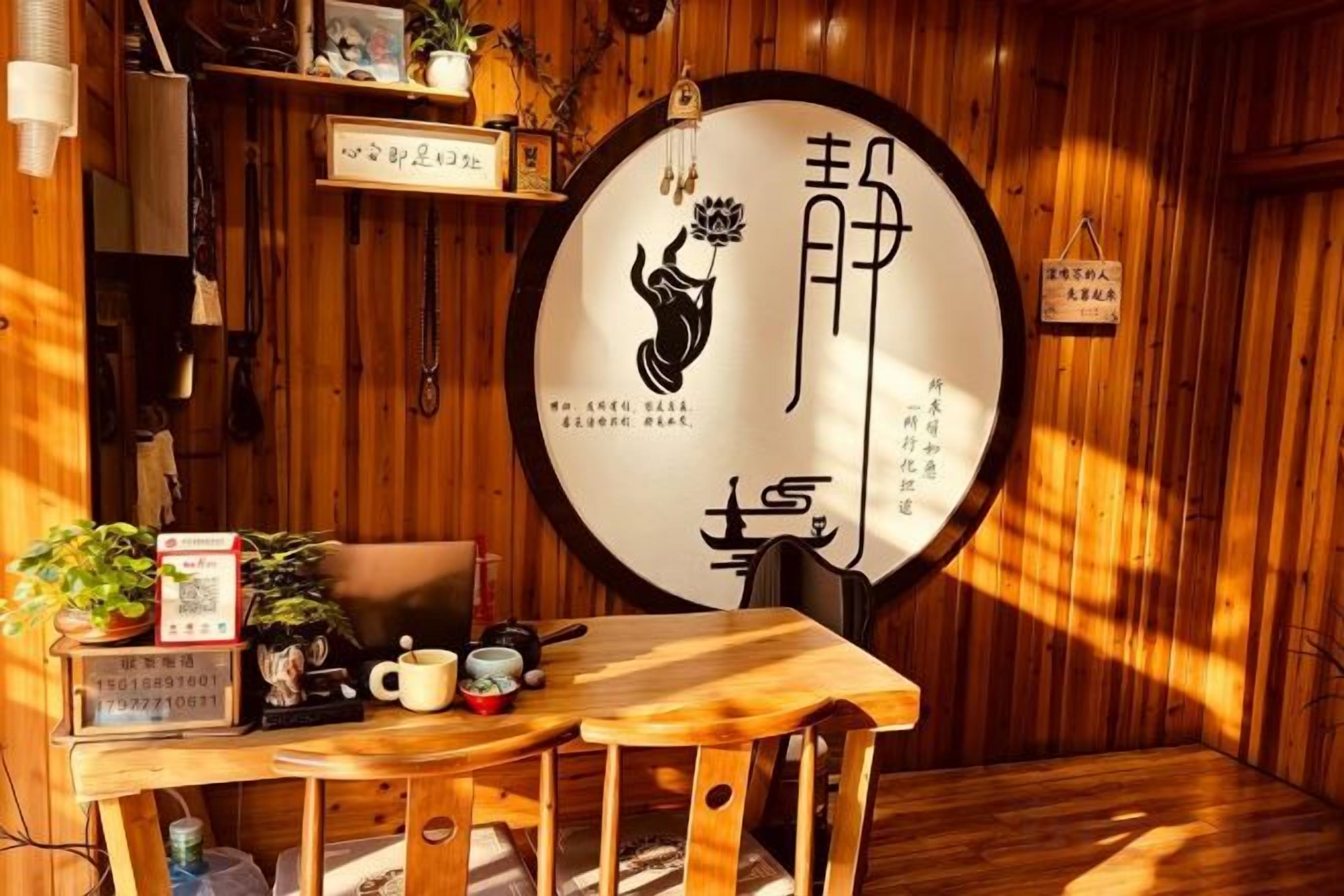 A wooden interior with a round wall hanging, a table with a teapot, and a chair.