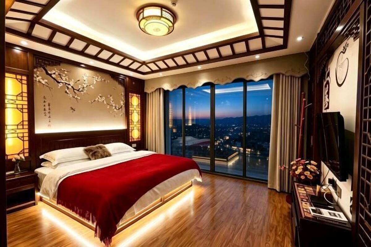 Ein Schlafzimmer mit großem Bett, Blick auf die beleuchtete Stadt bei Nacht und traditioneller Einrichtung.