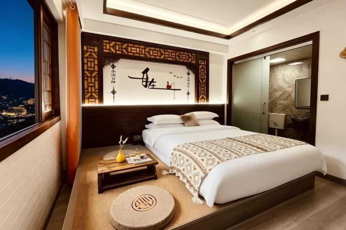 Ein modernes Hotelzimmer mit einem großen Bett, einem Nachttisch, einem kleinen Hocker und Blick auf die Stadt.
