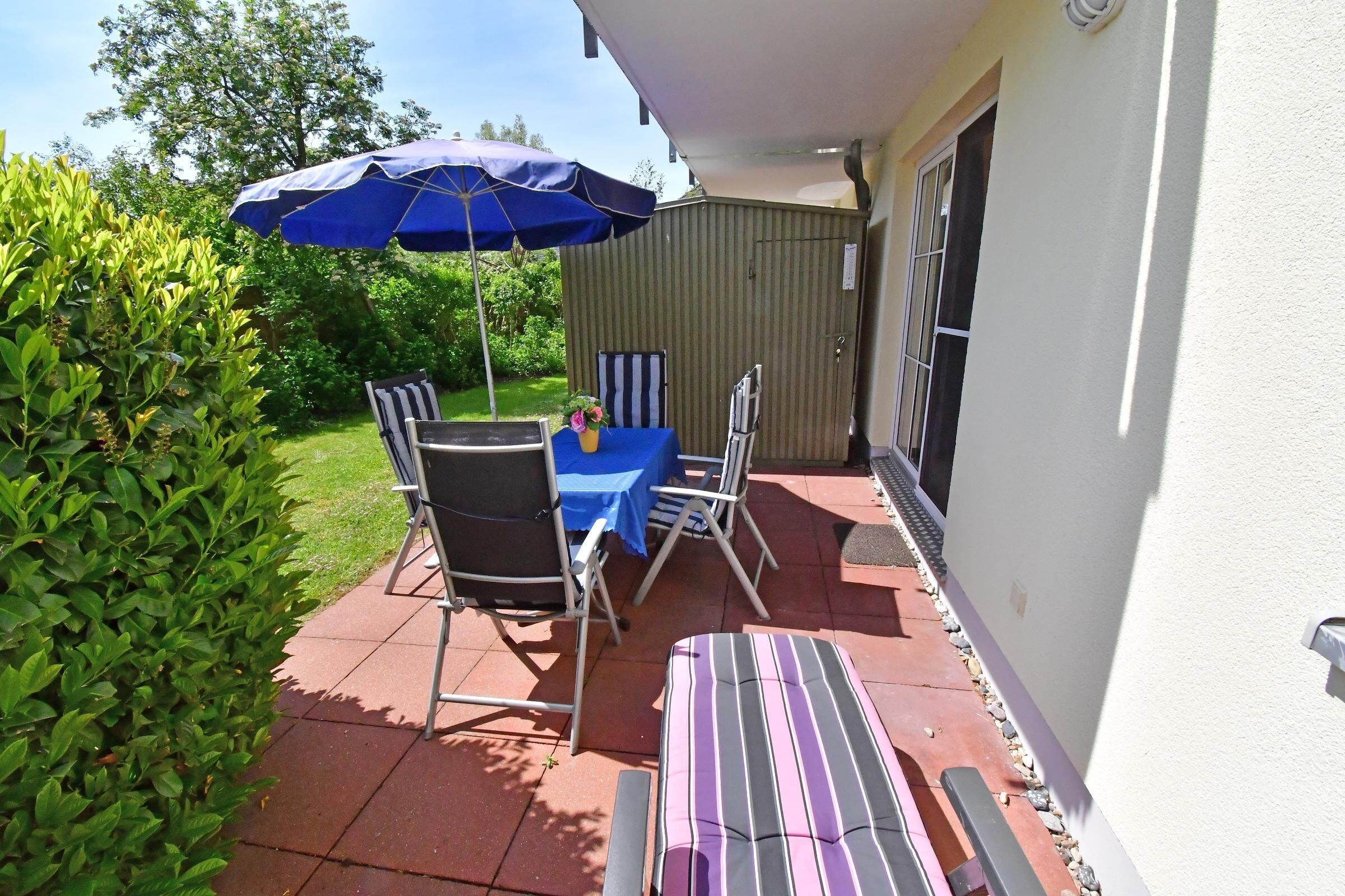 Un patio exterior con mesa, sillas y una silla reclinable a rayas.