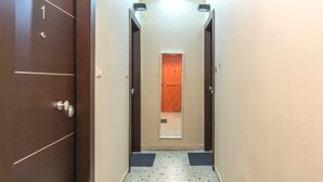Un couloir étroit, avec une porte en bois marquée du chiffre « 1 » sur le côté gauche, un luminaire au-dessus et une autre porte en bois au fond.