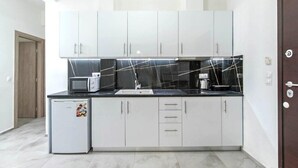 Une cuisine de taille réduite avec des meubles blancs, un plan de travail noir et un petit réfrigérateur.