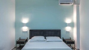 Une chambre à coucher comprenant un lit, deux tables de chevet, deux lampes fixées au mur et un appareil de climatisation.