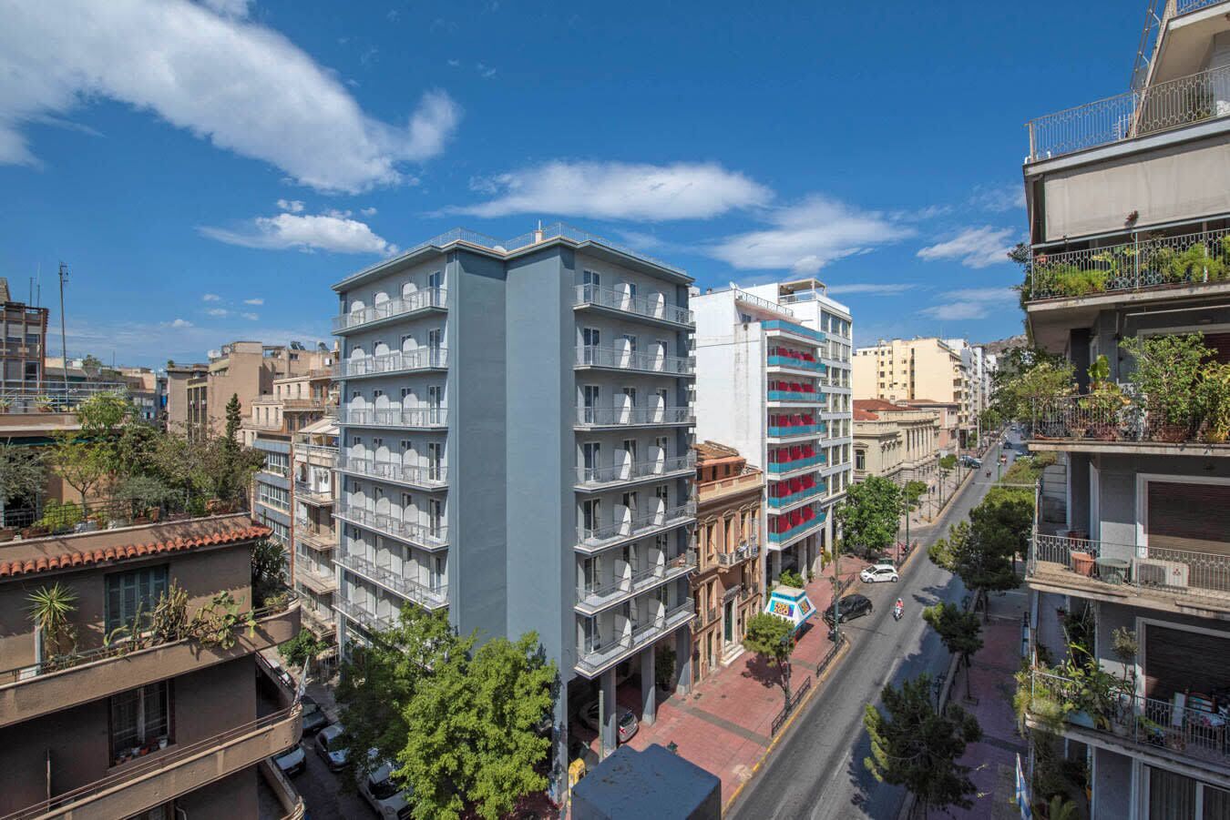Un immeuble à plusieurs étages doté de balcons, une rue au premier plan et d’autres bâtiments en arrière-plan.