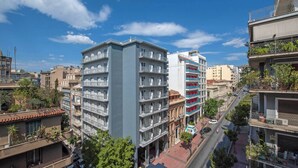 Un immeuble à plusieurs étages doté de balcons, une rue au premier plan et d’autres bâtiments en arrière-plan.