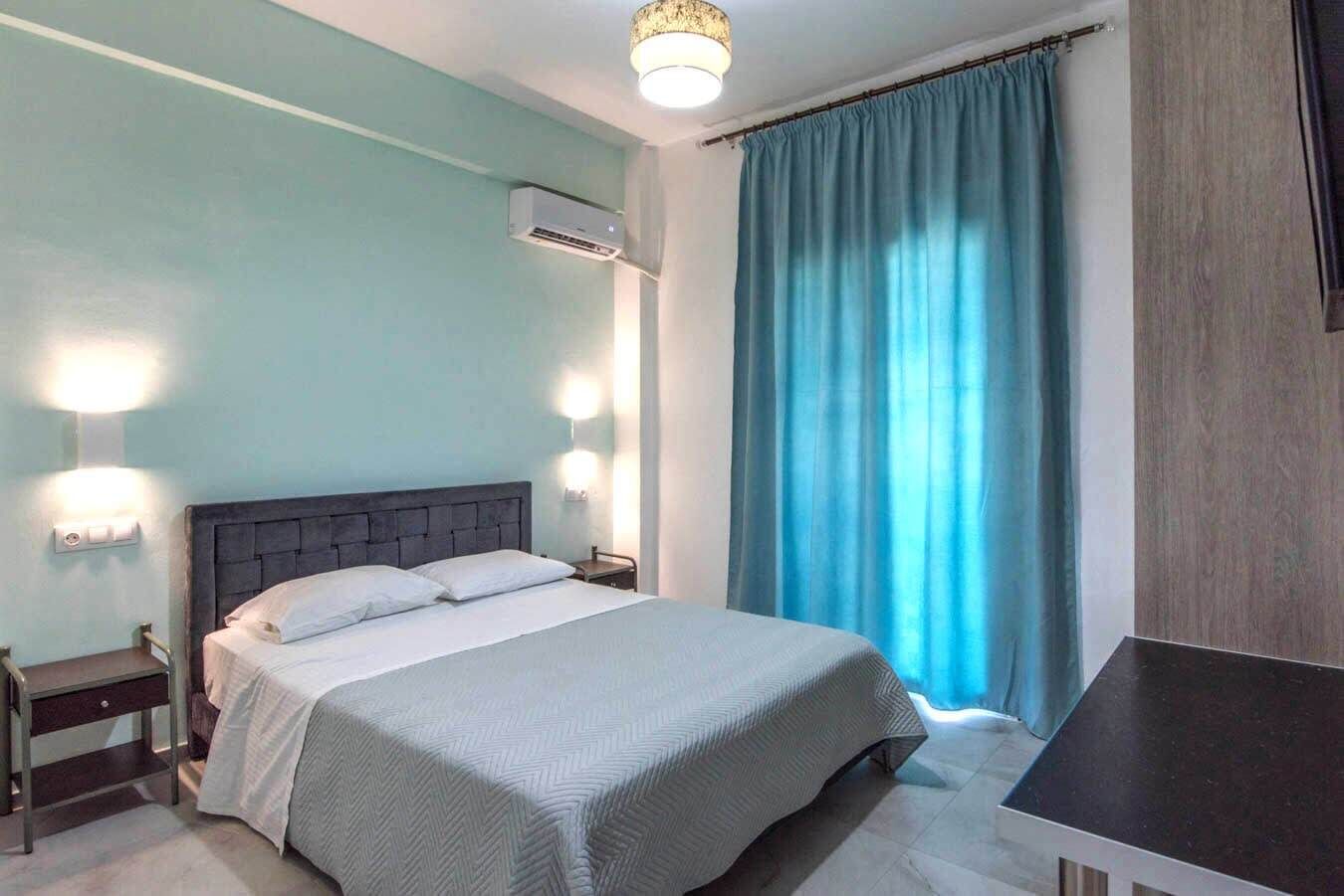 A bedroom with a bed, bedside tables, an air conditioning unit, and a curtain.