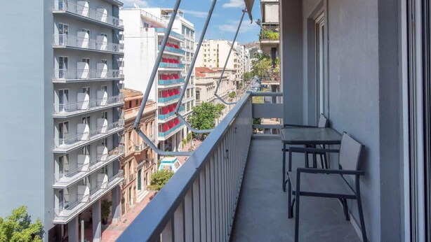 Un balcon avec une table et des chaises, donnant sur un paysage urbain composé d’immeubles à plusieurs étages et de balcons.