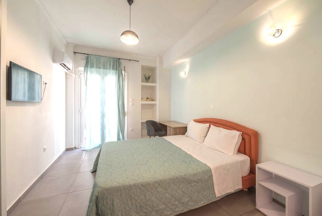 Un dormitorio con cama, escritorio, silla, televisor y estante.