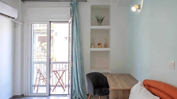 A bedroom with a bed, a desk, a chair, a balcony with a table, and a shelf with decorative items. - Sweet apartment in Athens A3 (Athina)