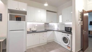 A compact kitchen with white cabinets, a built-in washing machine, a microwave, and a refrigerator. - Sweet apartment in Athens A3 (Athina)