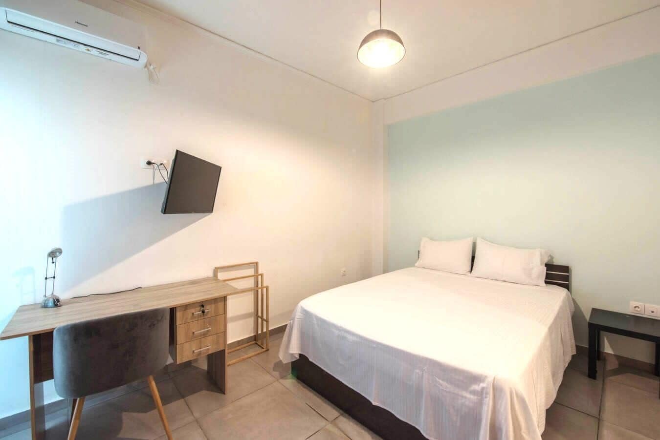 A bedroom with a bed, a desk, a chair, a TV, and a bedside table.