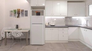 A modern kitchen with white cabinets, a built-in refrigerator, a dining table with chairs, and a small island with a sink and kettle. - Sweet apartment in Athens A3 (Athina)