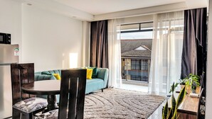 A modern living room with a sofa, a dining table, and a large window with curtains. - Affordable Spectacular Urban Stays (Nairobi)