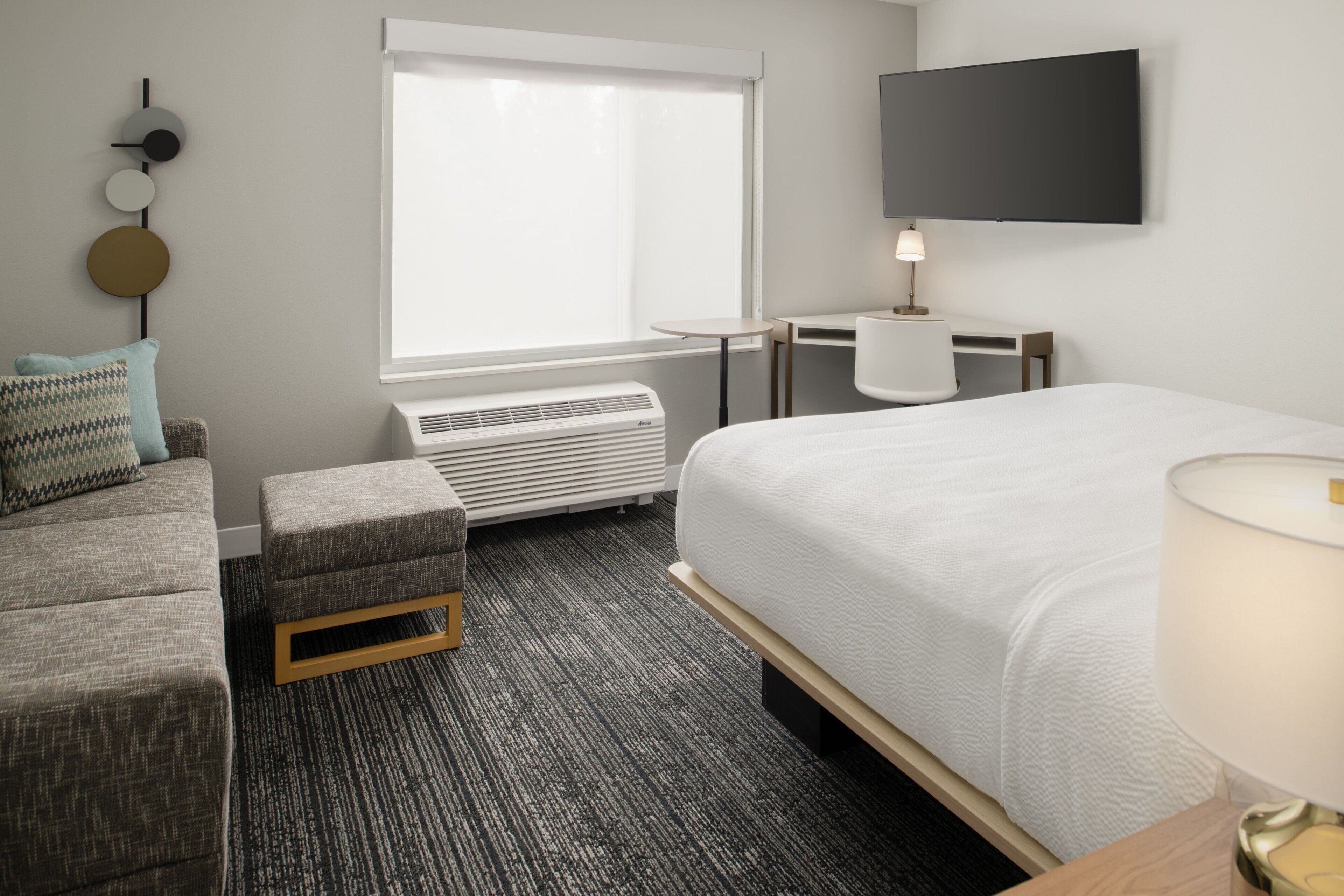 Une chambre d’hôtel équipée d’un lit, d’un bureau, d’une chaise, d’un canapé, d’un radiateur et d’un téléviseur fixé au mur.