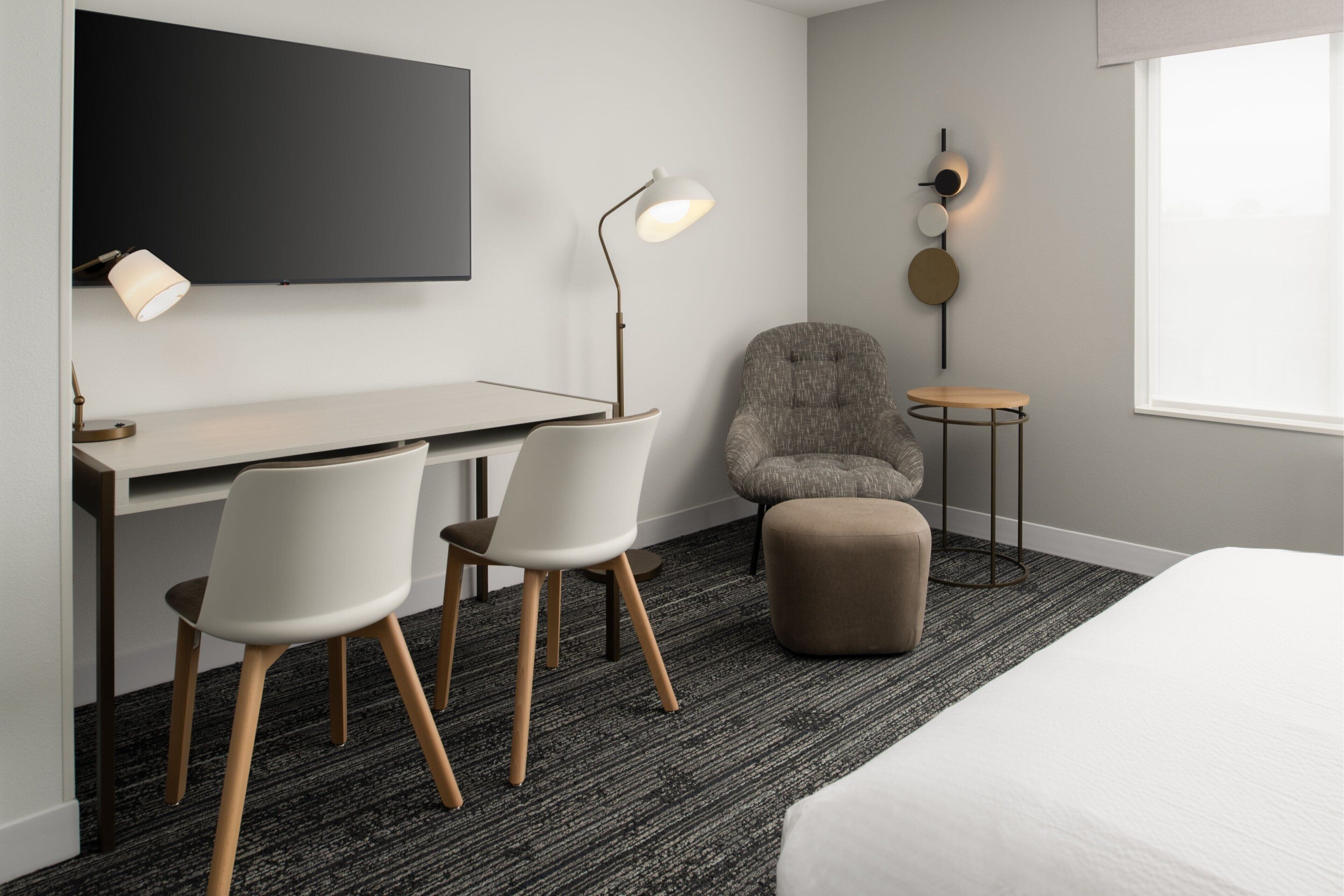 Une chambre d’hôtel moderne équipée d’un bureau, de deux chaises, d’un canapé, d’une petite table et d’un téléviseur fixé au mur.