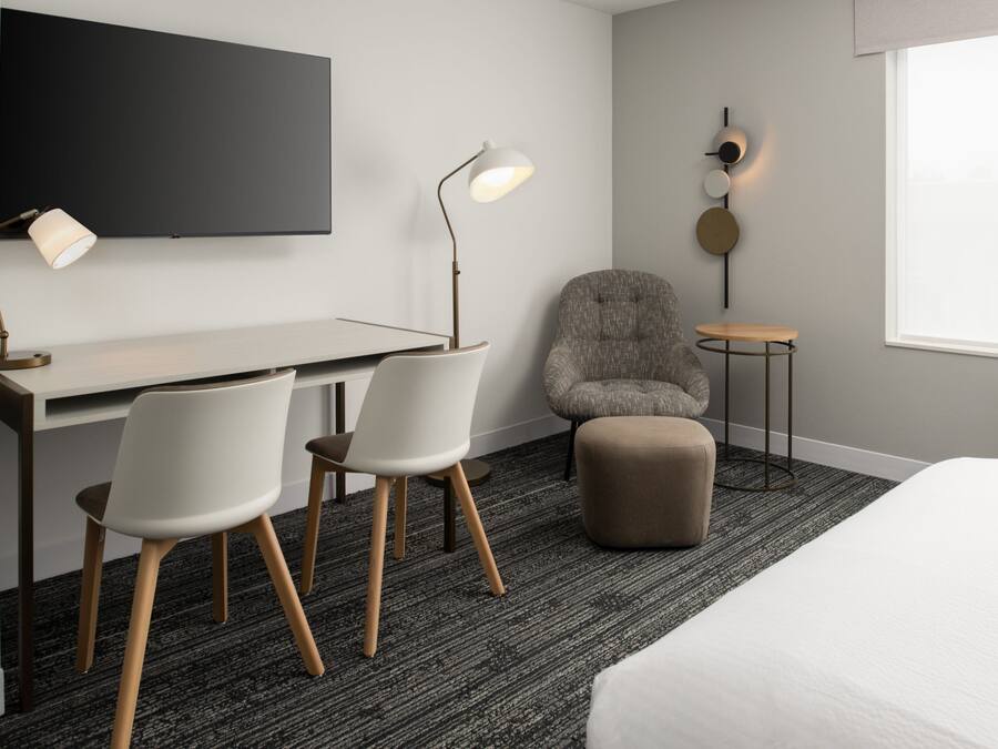 Una habitación de hotel moderna con un escritorio, dos sillas, un sofá, una mesita y un televisor montado en la pared.