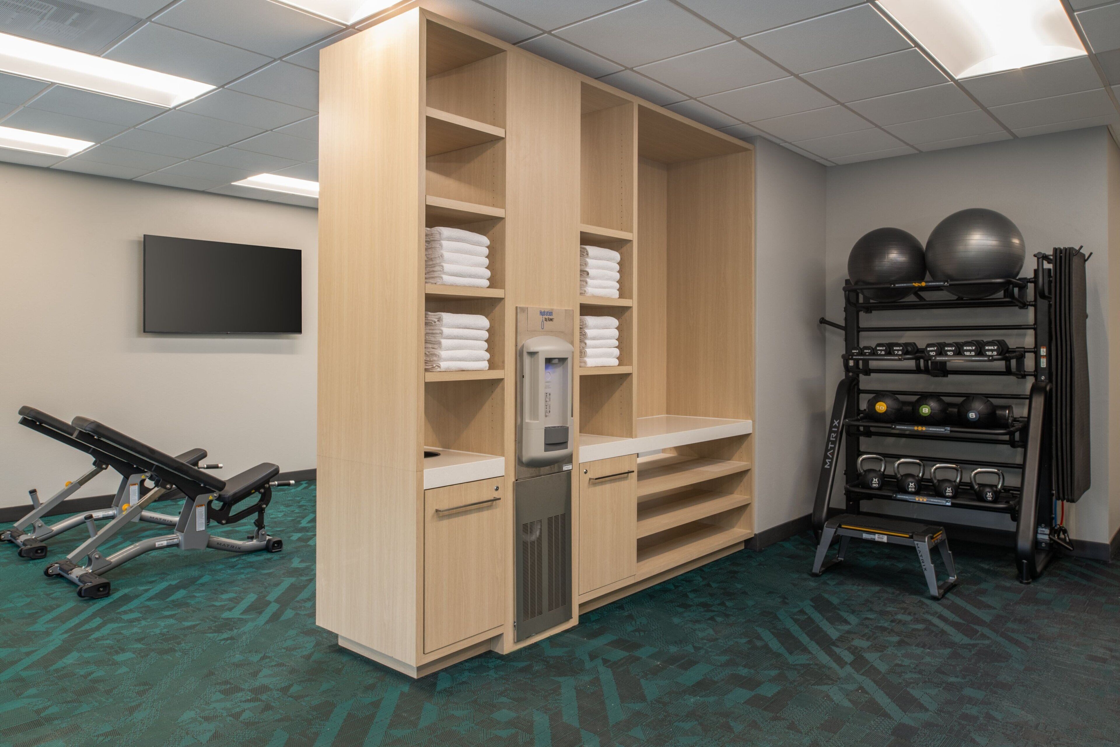 A gym with wooden cabinets, a water dispenser, exercise equipment, and a rack with exercise balls and weights.