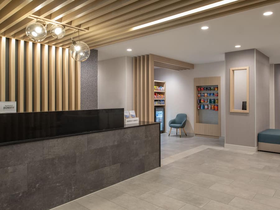 A reception area with a black reception desk, a wooden slatted ceiling, and a seating area with a blue chair and ottoman.