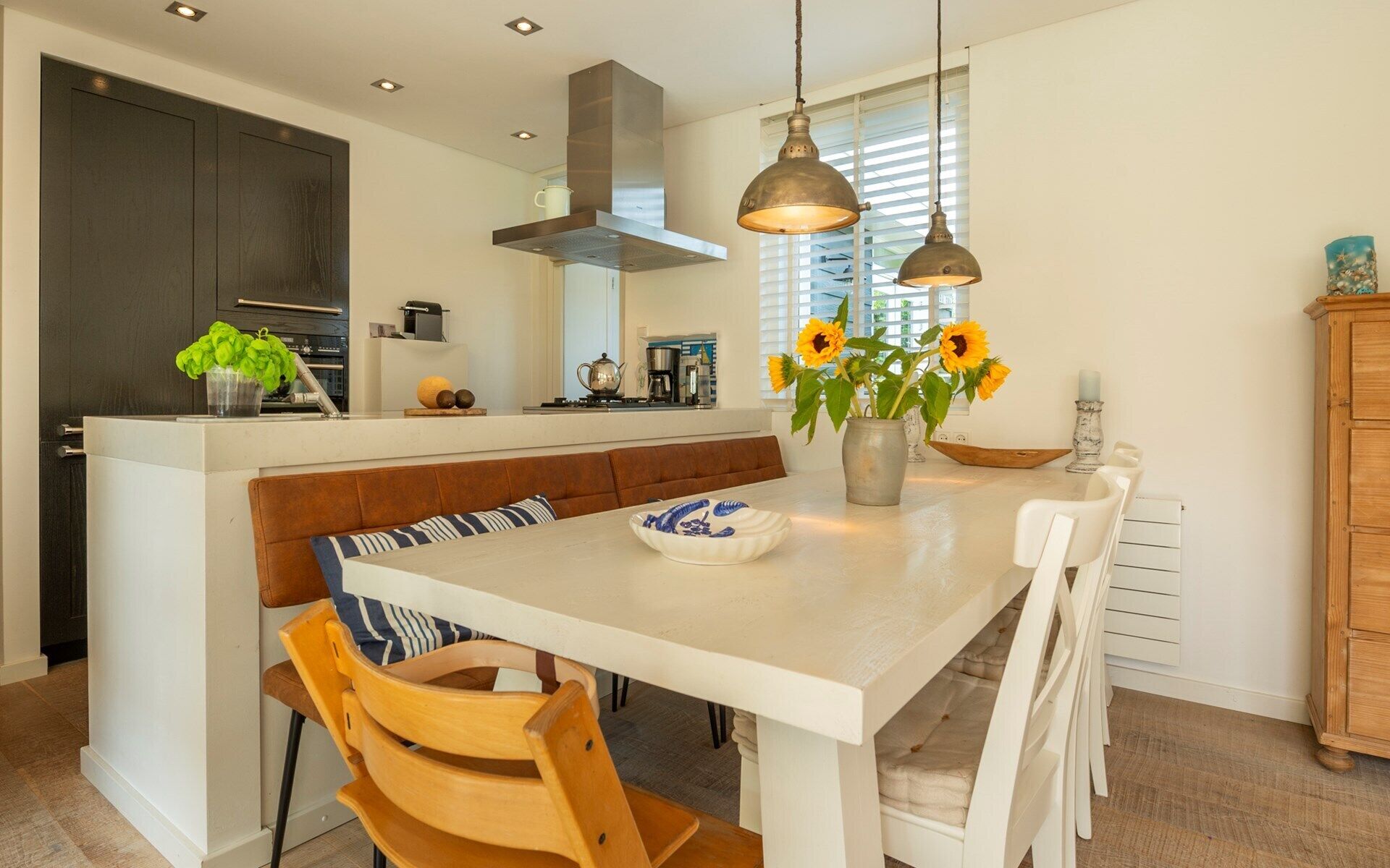 A modern kitchen with a central island, wooden chairs, and a bench.