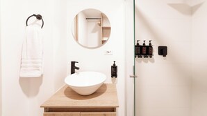 Une salle de bain moderne avec un meuble-lavabo en bois, un miroir rond, un porte-serviettes et une douche dotée d’une porte en verre.