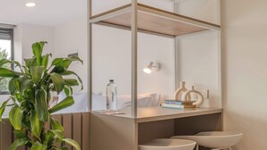 Une salle de bain moderne avec un grand miroir, une plante, une bouteille d’eau et deux tabourets blancs.