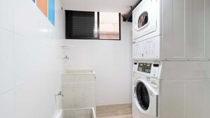 Une buanderie équipée d’un lave-linge et d’un sèche-linge superposés, d’un petit évier et d’une fenêtre située au-dessus du sèche-linge.