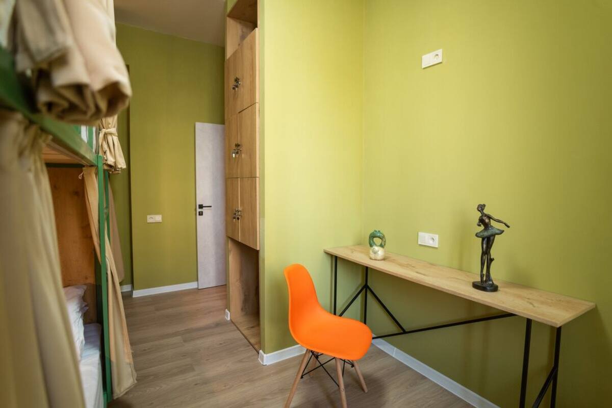 A room with a wooden desk, an orange chair, a green vase, and a ballet dancer statue.