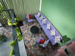 A covered outdoor seating area with a long table and chairs, a round table, and a patterned floor. - La Casa EmilioAngi (Yerevan)