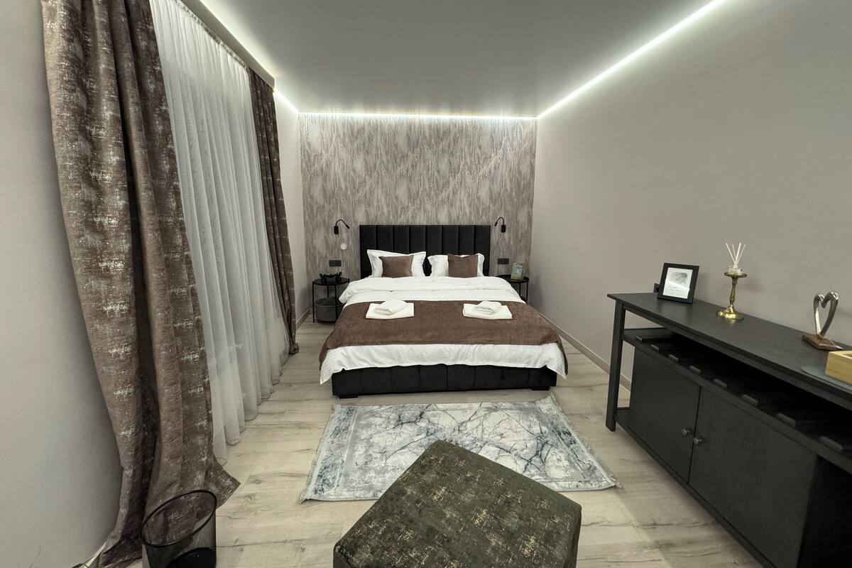 A modern bedroom with a large bed, a bedside table, a bench, and a wardrobe.