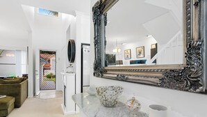 Une salle de bain moderne avec un grand miroir décoratif, un comptoir en marbre et une vue sur l’espace de vie, visible à travers le miroir.