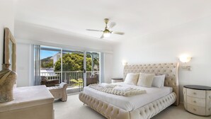 Une chambre spacieuse avec un grand lit, un ventilateur de plafond, une vue sur l’extérieur et un balcon.