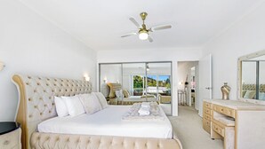 Une chambre spacieuse avec un grand lit, une coiffeuse avec un miroir et un ventilateur de plafond.