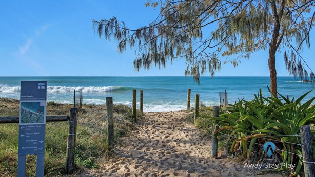 Un sentier de sable qui longe la plage et mène à l’océan, avec un panneau indiquant les directions vers différentes plages.