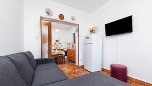 Un salon avec un canapé gris, un pouf rouge et un téléviseur fixé au mur.