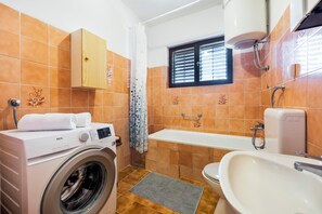 A compact bathroom with a washing machine, a bathtub, and a sink. - Apartment Eda (Rovinj)