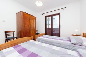 A bedroom with two beds, a wooden wardrobe, a chair, and a small table with a lamp. - Apartment Eda (Rovinj)