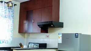 A kitchen with wooden cabinets, a stainless steel refrigerator, and a black range hood. - Claris Cozy Homes Near US Mall (Kampala)
