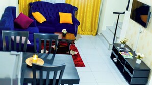 A living room with a blue sofa, red rug, and a TV on a stand. - Claris Cozy Homes Near US Mall (Kampala)
