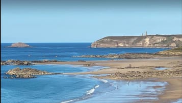 Experience the serene coastal landscape with gentle waves and a historic lighthouse in the distance.