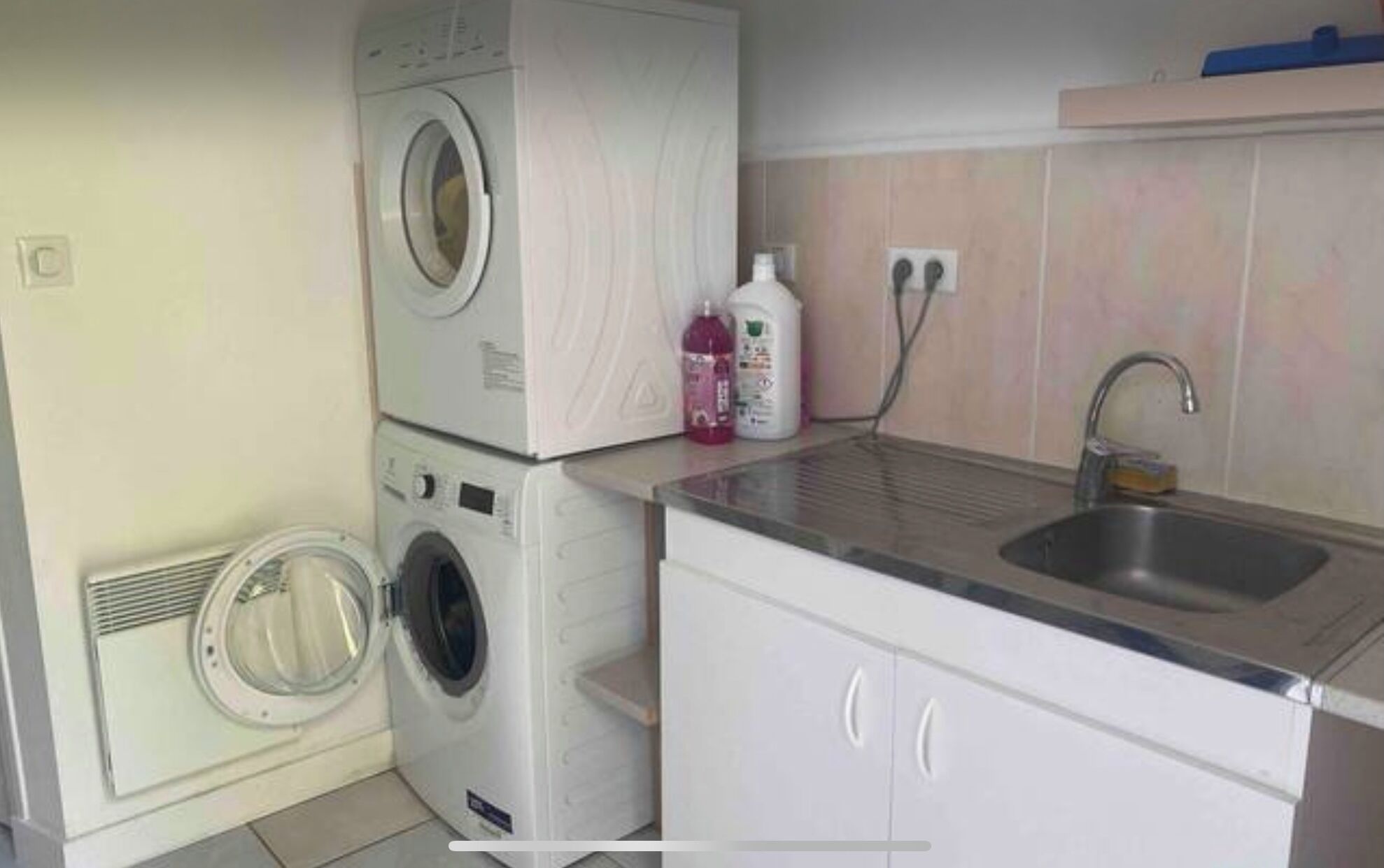 A compact laundry area with stacked washing machines, a sink, and cleaning supplies.