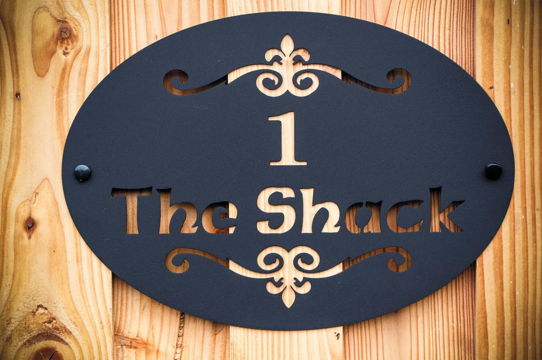 Ein Holzschild mit der Aufschrift "1 The Shack", in Holz geschnitzt und auf einem Holzhintergrund befestigt.