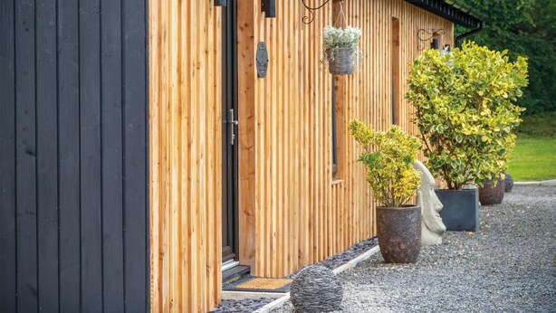 A wooden building with a door, a hanging basket, and potted plants. - The Shack - 1 Bedroom - Cosheston (Pembroke)