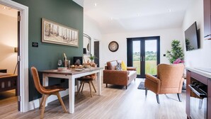 A modern living room with a dining area, a fireplace, and a large window with a view. - The Shed - 1 Bedroom - Cosheston (Pembroke)