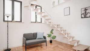 A modern living room with a grey sofa, a floor lamp, a staircase, and a potted plant. - Vista Napoli Residence (Naples)