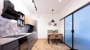 A modern kitchen with a herringbone wood floor, a built-in oven, and a herringbone tile backsplash. There is a dining area with a table and chairs, and a large sliding glass door leading to a balcony. - Native Apartments Pułaskiego 6 (Kraków)