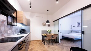 A modern kitchen with a wooden cabinet, a coffee machine, and a dining area with a table and chairs. - Native Apartments Pułaskiego 6 (Kraków)