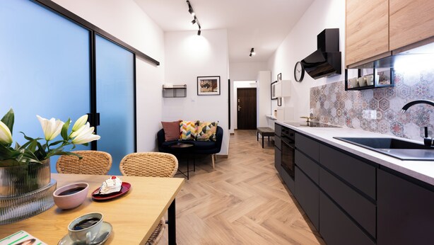 A modern kitchen with a large island, a dining area with a table and chairs, and a living space with a sofa and cushions. - Native Apartments Pułaskiego 6 (Kraków)