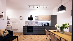 A modern kitchen with a herringbone wood floor, a dining area with a wooden table and wicker chairs, and a black pendant light. - Native Apartments Pułaskiego 6 (Kraków)