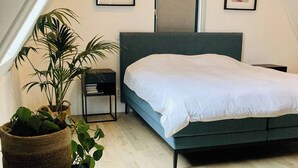 Ein Schlafzimmer mit einem Bett, einem Nachttisch, einer Topfpflanze und gerahmten Bildern an der Wand.