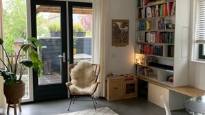 Ein modernes Wohnzimmer mit einer großen Bücherwand, einem gemütlichen Sessel, einem kleinen Tisch und einer Topfpflanze.